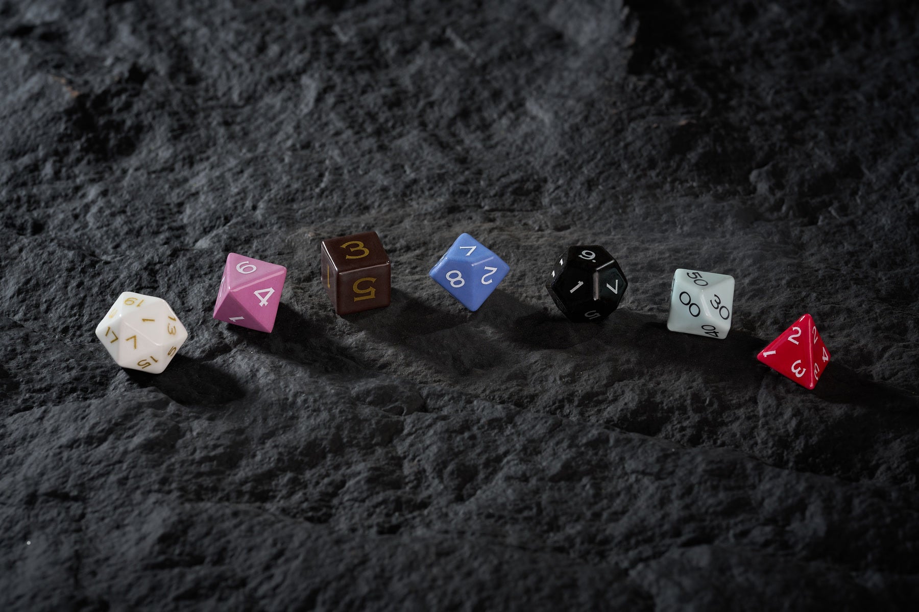 Colorful ceramic polyhedral dice arranged across textured stone