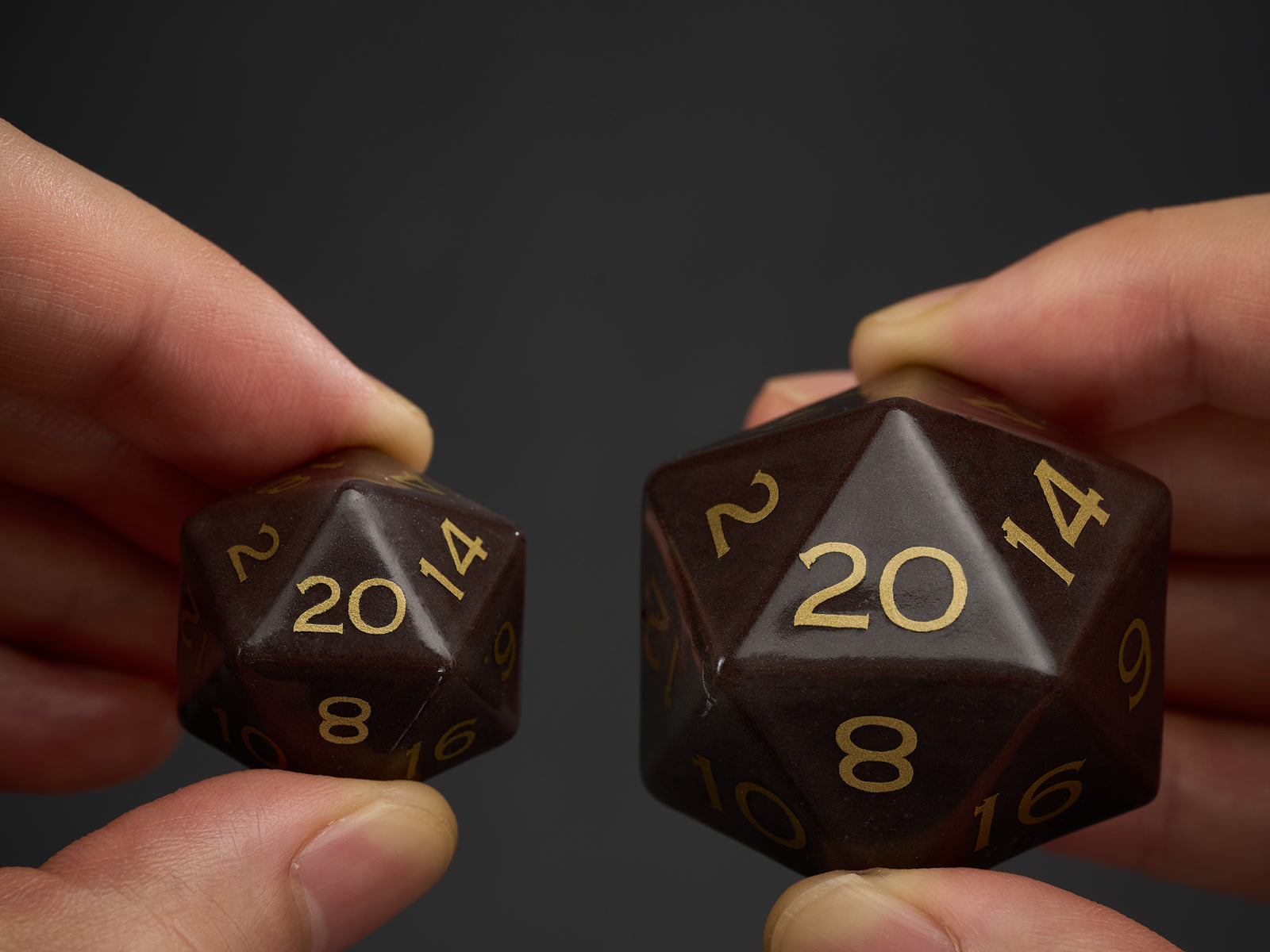 A 23 millimeter and a 36 millimeter brown ceramic D20 held side by side for scale